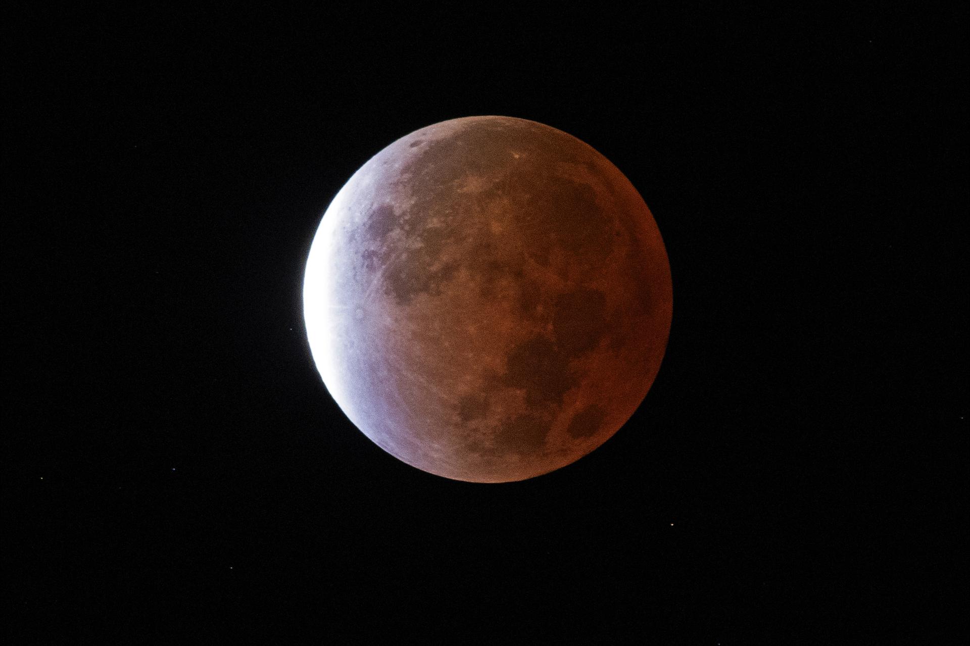 A deep partial lunar eclipse with most of the Moon copper-red and a bright uneclipsed crescent
